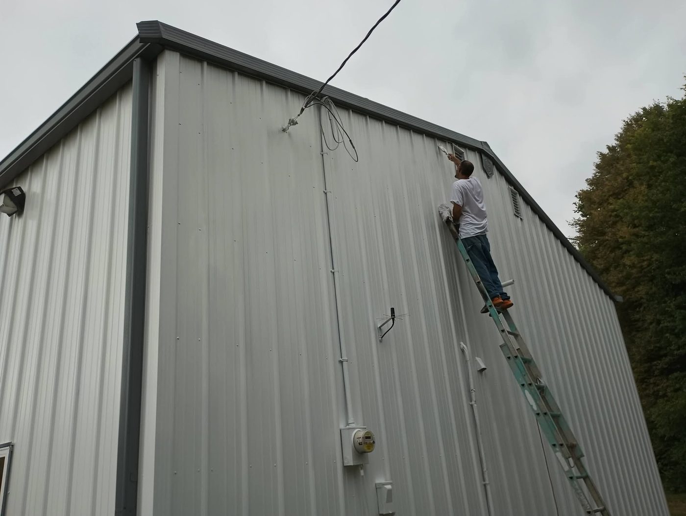 Painter on a ladder cutting in trim on a metal building